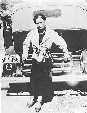 Black and white photograph of Bonnie Parker leaning against the back of the car.