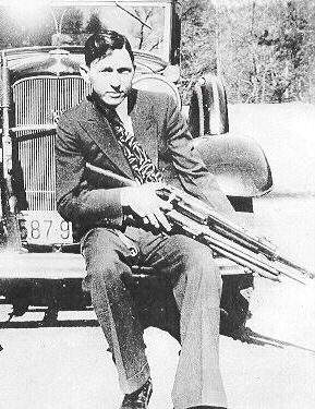 Black and white photograph of Clyde Barrow leaning against the front of his car.